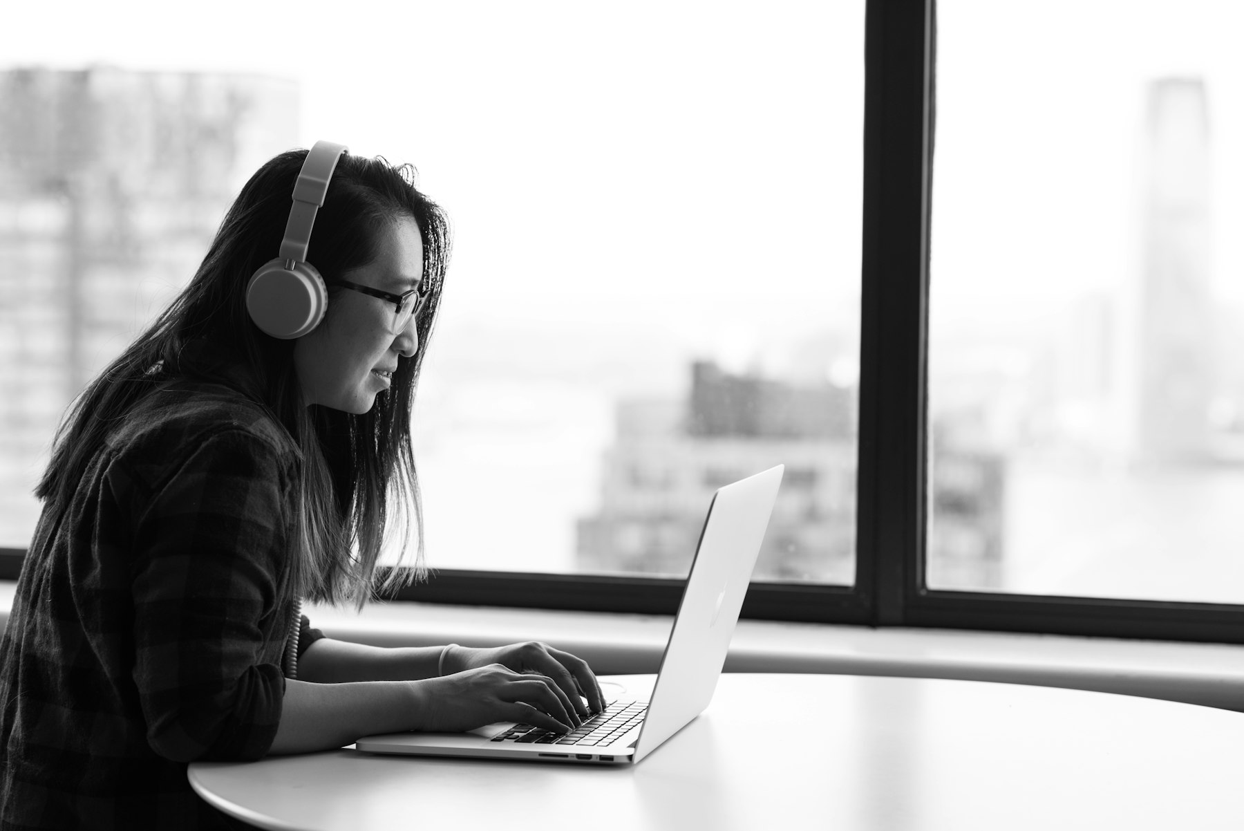 A person wearing headphones works on a laptop beside a window.