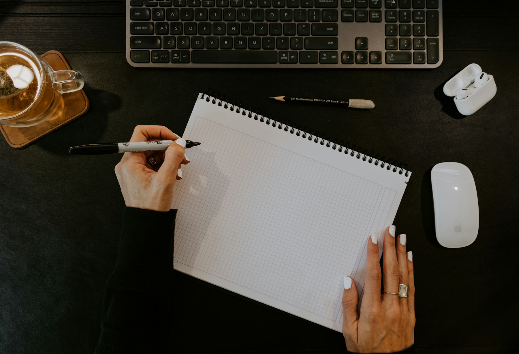 Hands begin a sketch in a grid notebook on a desk.